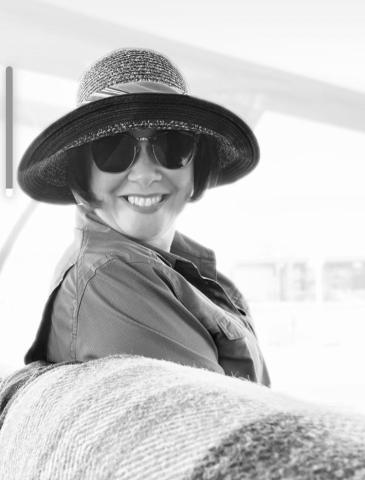 Head and shoulders of smiling white woman wearing dark brimmed hat and sunglasses. Black and white.