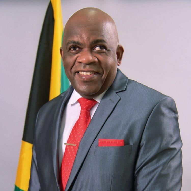 Senator Morris smiling with a Jamaica flag in the background