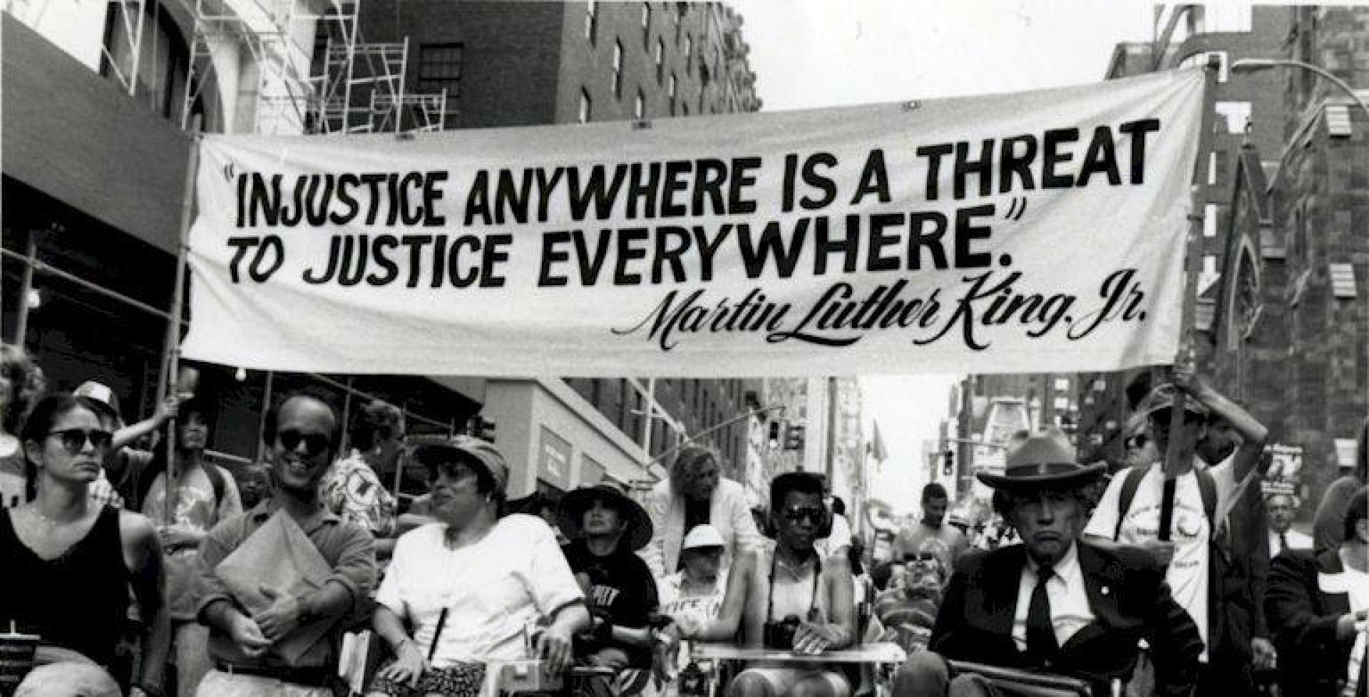 1993 march in New York City. At front are Paul Miller, Judy Heumann, Justin Dart. Holding a sign that says: "Injustice anywhere is a threat to justice everywhere."